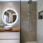 Bathroom renovation completed by Turul Building Services - A modern bathroom with large dark tiles, round backlit mirror, a half-open shower cabin with dual shower head in two sizes