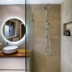A modern half-open shower cabin separated from the bathroom by a glass panel, large dark tiles and a dual shower head | Recent bathroom renovation by Turul Building Services