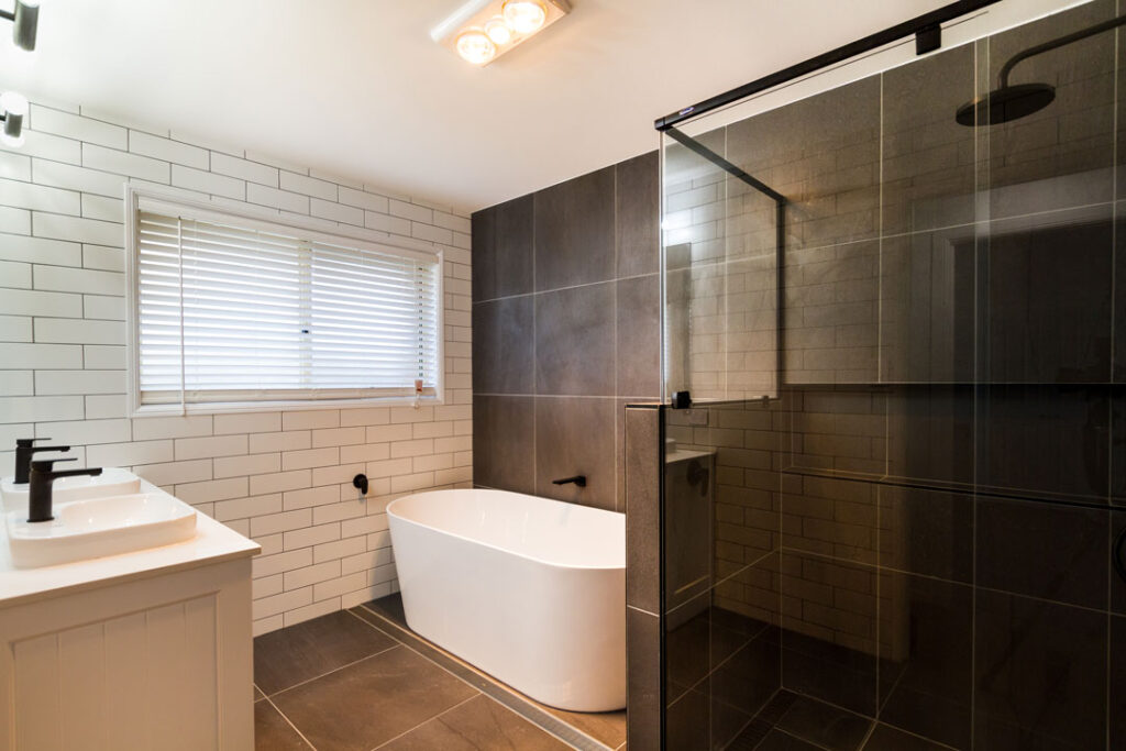 A modern bathroom with a dark tint glass shower screen, contemporary bathtub and dual sinks.