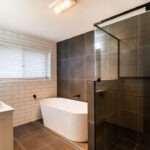 A modern bathroom with a dark tint glass shower screen, contemporary bathtub and dual sinks.